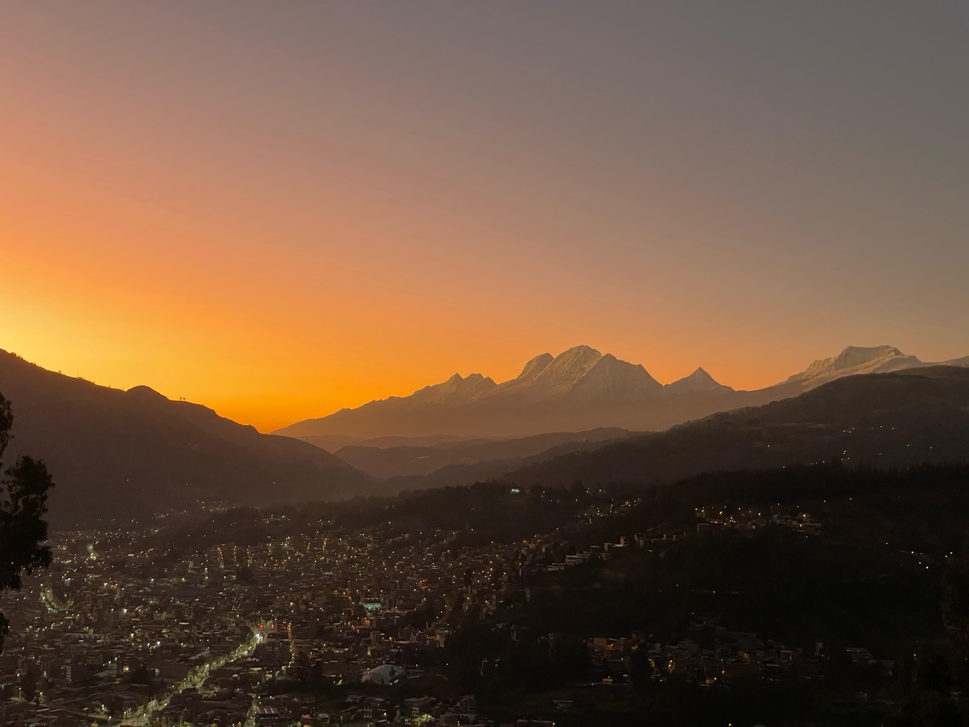 The city of Huaraz glowing at dusk in a valley below the snow-capped peaks of the Cordillera Blanca at sunset, Peruvian Andes